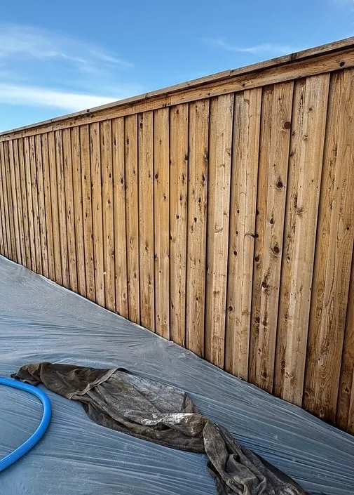 New cedar fence before staining, with plastic sheeting laid along the base