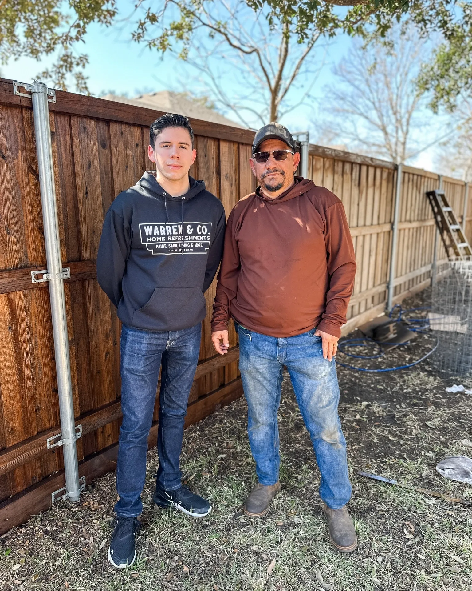Noah Warren, owner, and Gustavo, lead restoration specialist, standing in front of a freshly stained cedar fence