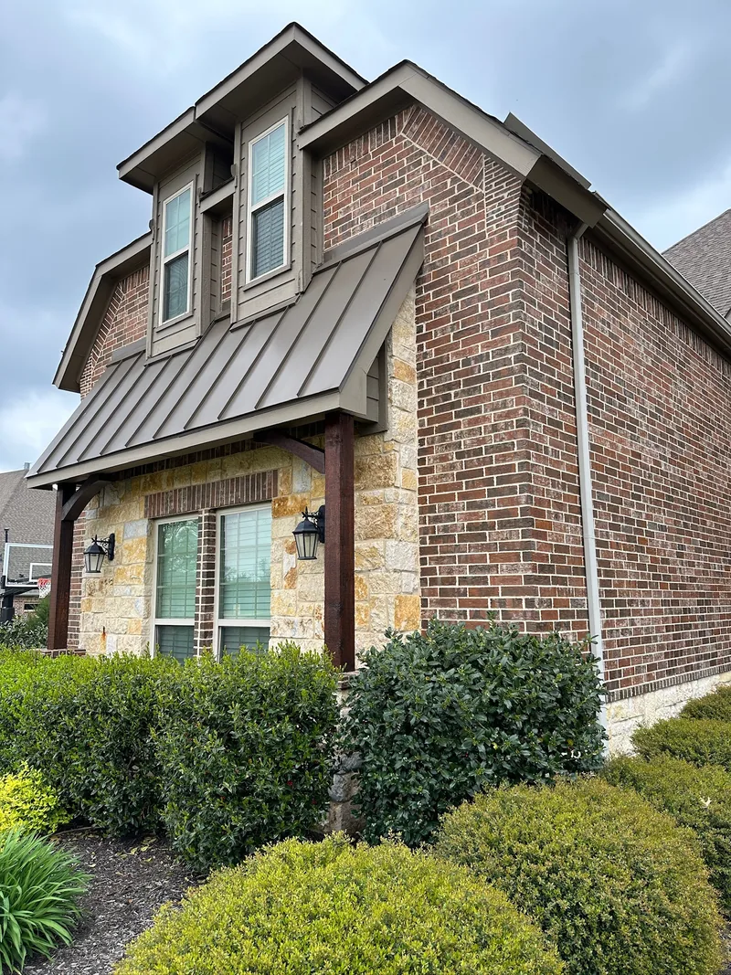 Brick and stone home with painted trim, dormers and a dark metal awning